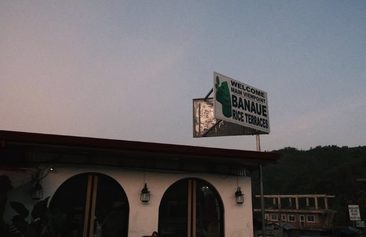 The Banaue main viewpoint sign at dusk, lit windows in the building below it