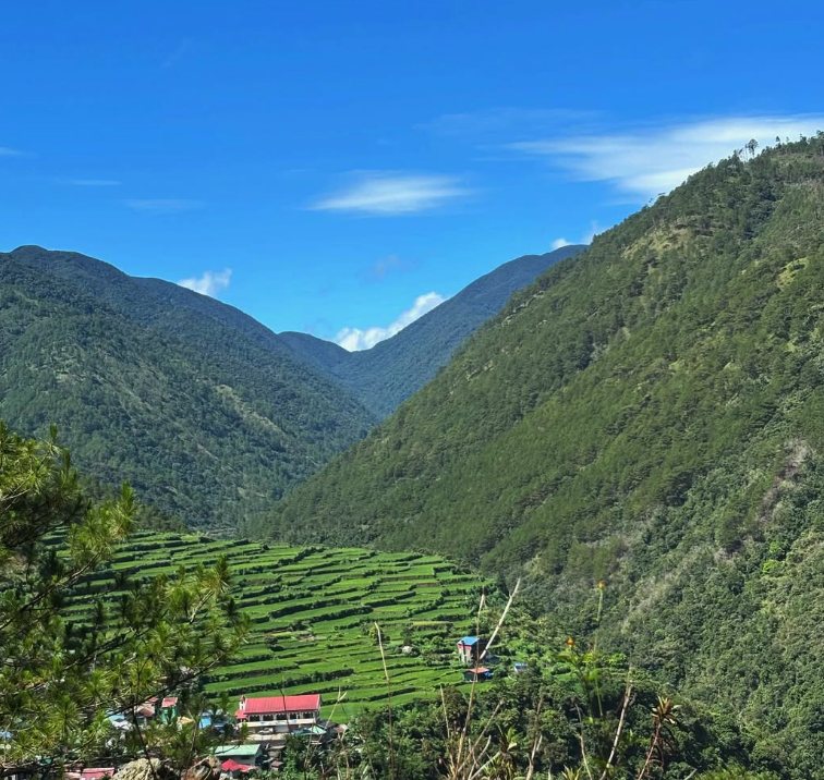 A wide forested valley with terraces and a small village on the floor beneath the ridge line