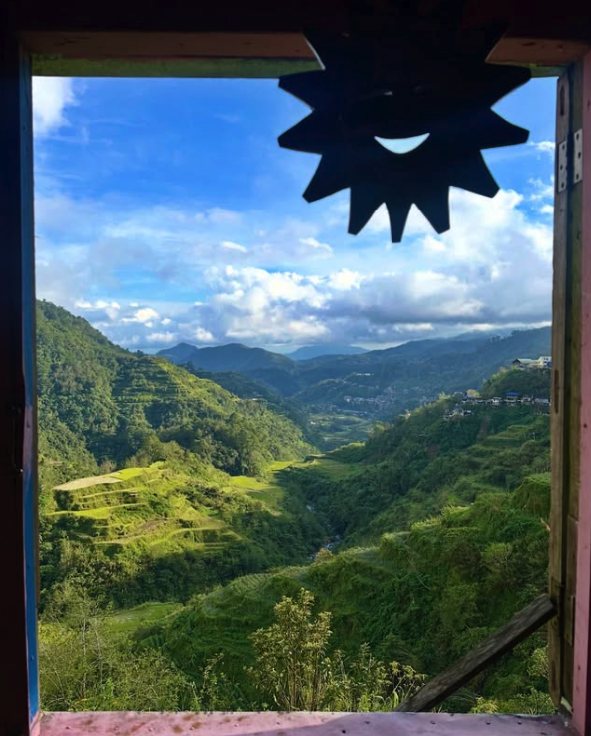 The Banaue valley framed by an open guesthouse window with a carved wooden sun hanging in the doorway