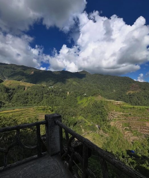 A stone and timber viewing deck above the valley, with terraces on the far slope under building cloud